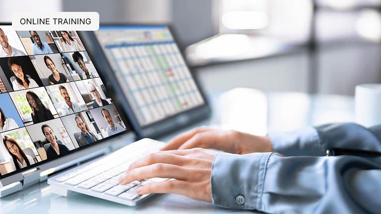A man typing on keyboard with two screens in front of him. One is of an online business videoconferencing and the other has a spreadsheet pulled up.