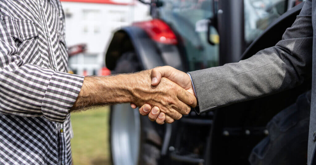 Two men shaking handsin front of tractor